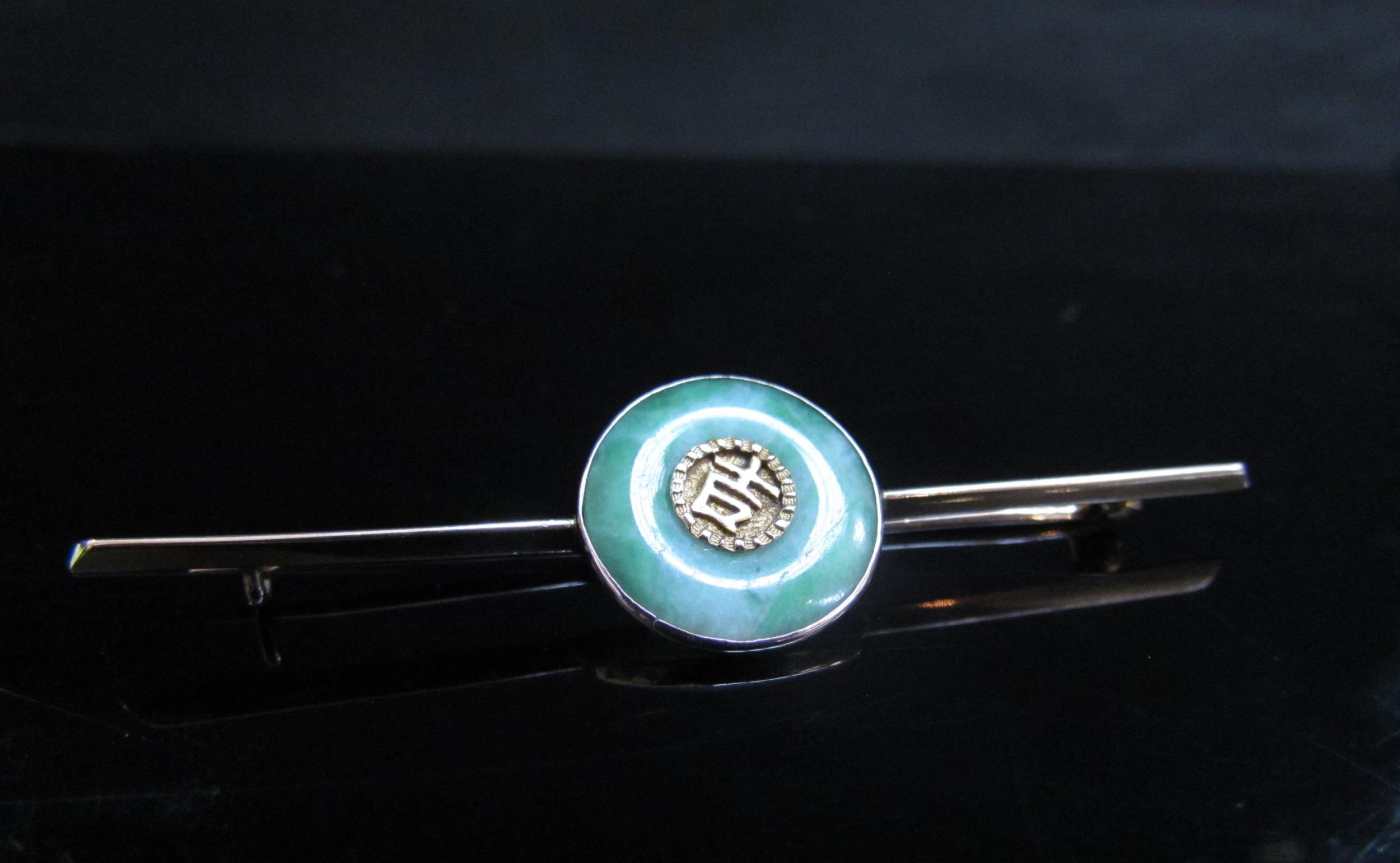 A Chinese gold bar brooch centrally set with a jade roundel with character mark to centre, 7cm long,