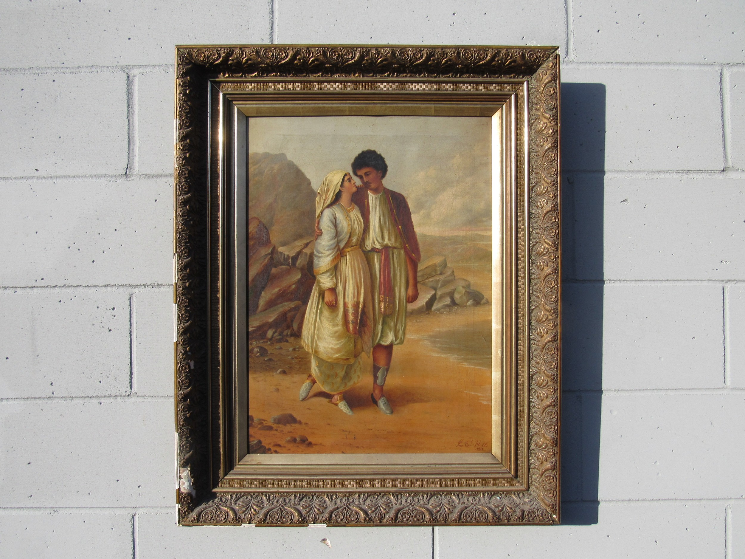 A late 19th Century oil on canvas depicting an Eastern couple standing on a shore, mountain rocks