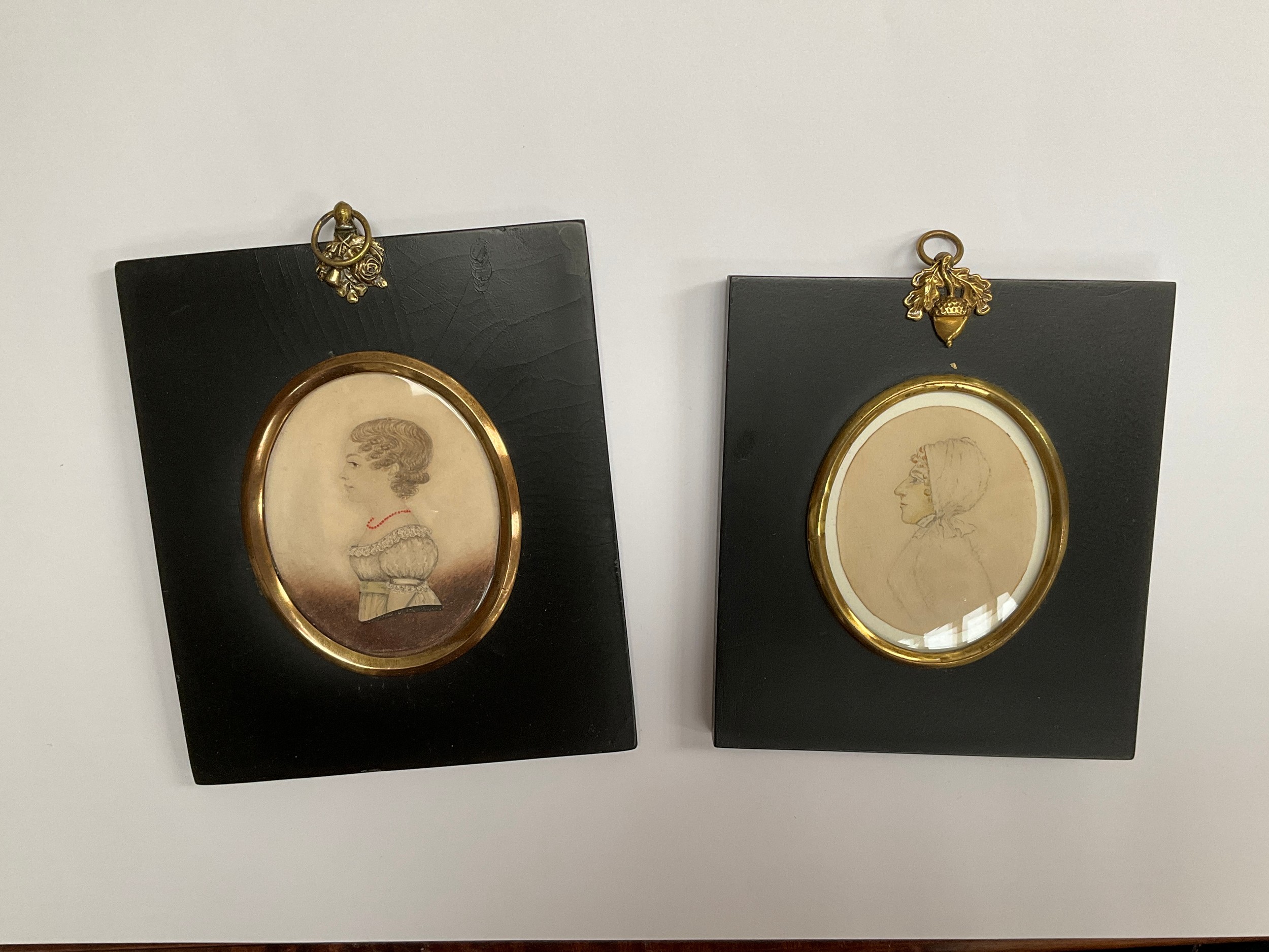 Two oval mounted miniature portraits on paper in ebonised frames with acorn and floral hangers.
