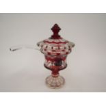 A ruby and clear glass pedestal jar and cover with ladle, 30cm tall