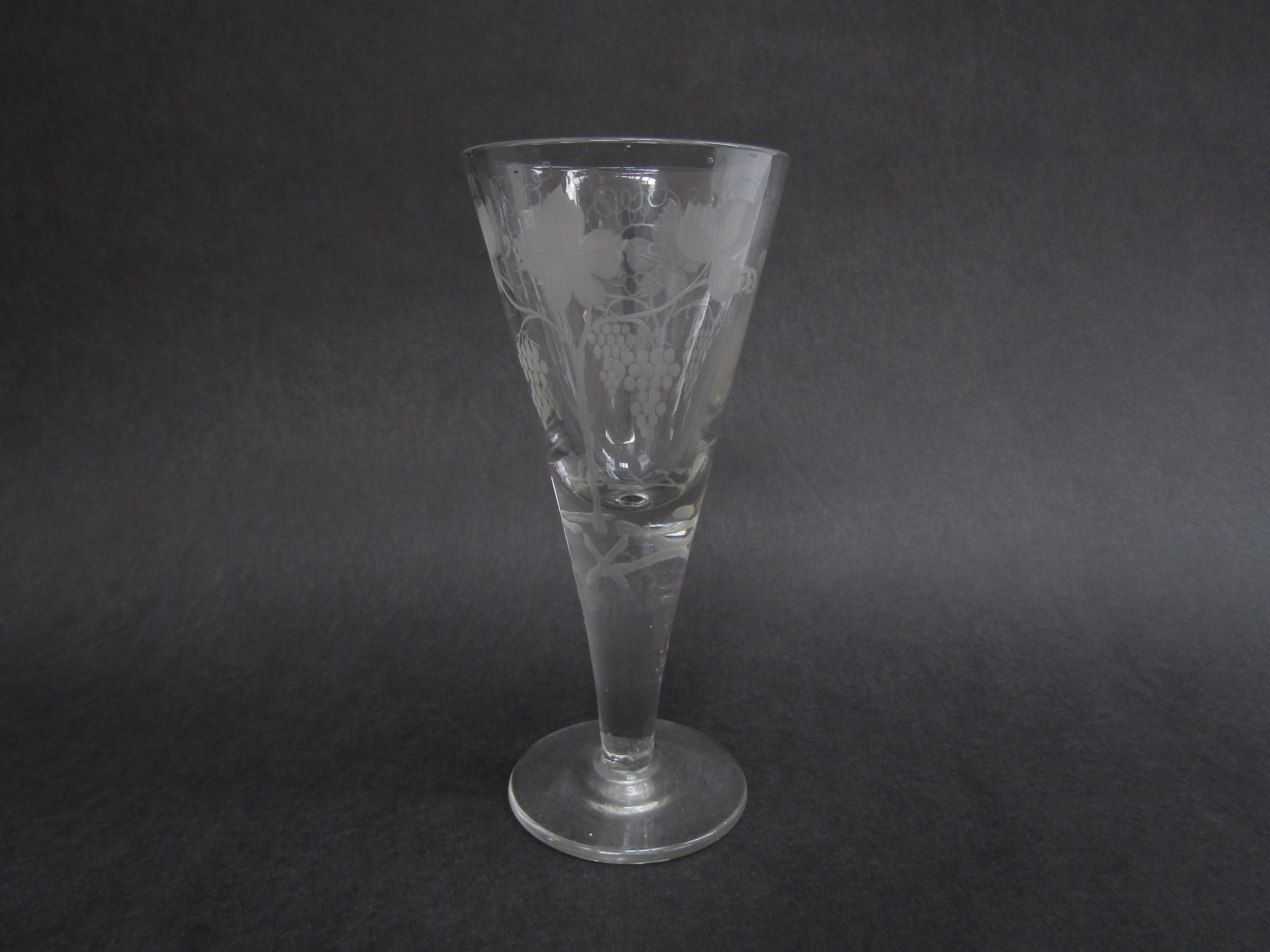A late 19th Century conical ale glass with etched grape and vine detail, circular foot, 21cm tall