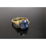 An 18ct gold ring, the central oval sapphire 10mm x 8mm flanked by diamonds in rubover setting. Size