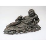 An Eastern hardwood sculpture of recumbent figure with dragon on fitted base, 21cm tall x 40cm