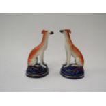 A pair of 19th Century Staffordshire whippets seated on blue bases with gilt detail, 10cm tall
