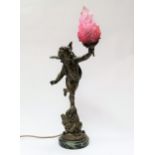 An early 20th Century bronzed spelter table lamp of cherub form, holding cranberry flame glass torch