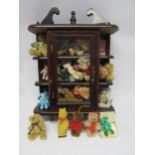 A glazed front wooden collectors cabinet (44cm tall) containing a collection of miniature teddy