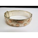A silver engraved stiff hinge bangle with motifs in gold of flowers, bird and butterfly, 47.5g