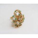 A gold dress ring with seven stacked circles each set with emeralds and diamonds on a textured