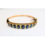 A gold sapphire and diamond stiff hinged bangle, the nine graduated oval sapphires spaced by two old