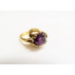 An 18ct gold ring with textured shank and scrolling tendrils holding an amethyst. Size O/P, 9.2g