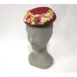 A 1950's puce coloured moulded hat bearing an array of faux flowers