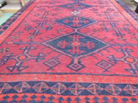 An Eastern red ground wool rug, four navy medallions to the centre, flanked by a mulitple border,