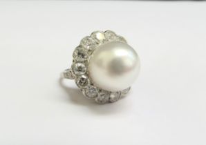 A platinum ring set with a large pearl 12mm diameter framed by fourteen diamonds, 1.40ct total