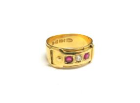 An 18ct gold buckle ring with single diamond flanked by rubies. Size L, 4.1g