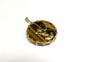 A tiger's eye circular pendant framed in a 9ct gold mount with gold Archer (Sagittarius) to