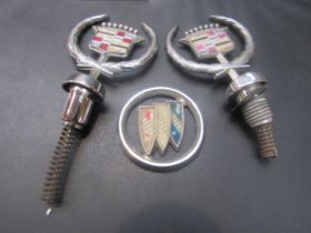 Two Cadillac raised bonnet crests and a Buick badge