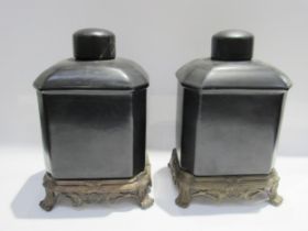 A pair of Oriental ceramic tea canisters on stands, black bodies of canted form with metallic footed