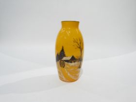 An orange glass vase depicting a silhouette of a log cabin, cartwheel and trees in a snowy