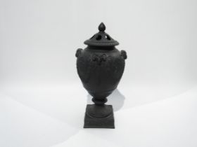A Wedgwood black basalt lidded urn with ram's head detail. The lid is damaged and nibble to rim,