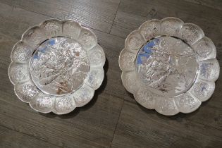 A pair of white metal scalloped form chargers with centres depicting Japanese warriors, 31cm