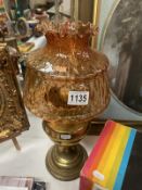 A brass oil lamp with amber coloured glass shade