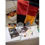 A box of East German ephemera including flags, car badges, pin badges, medalliion and postcards.