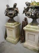 A pair of cast iron garden urns featuring cherubs and rams standing on pedestals. COLLECT ONLY.