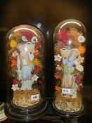 A pair of 19th century bisque porcelain figures under unrelated glass domes.