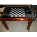 A chess table with glass top and storage compartment with contents.