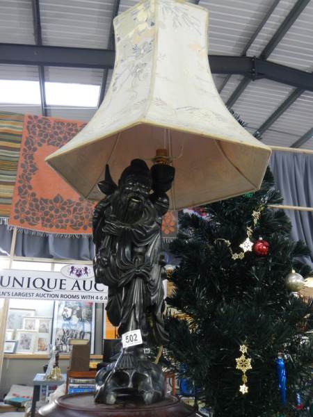 A carved wooden table lamp in the form of a Chinese gentleman complete with shade.