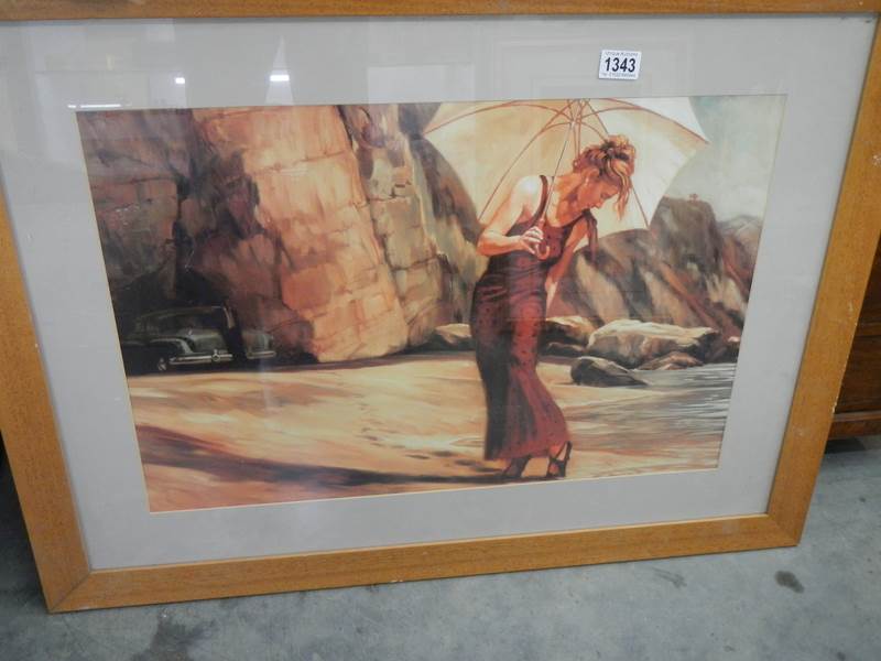 A framed and glazed beach scene featuring a lady with a parasol.