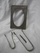 A silver photo frame, two silver sugar tongs and a silver pencil.