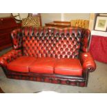 A 20th century deep buttoned blood red leather three seat winged sofa, COLLECT ONLY.