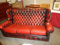 A 20th century deep buttoned blood red leather three seat winged sofa, COLLECT ONLY.