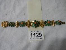A yellow metal bracelet with flower shapes in green stone with red centre's