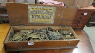 A wooden box containing brass furniture fittings.