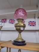 A Victorian brass oil lamp on ceramic base with Victorian cranberry glass shade, in good condition.
