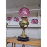 A Victorian brass oil lamp on ceramic base with Victorian cranberry glass shade, in good condition.