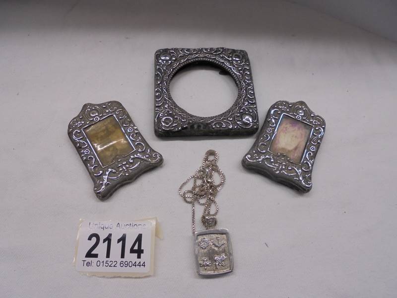 Three small silver photo frames and a silver pendant.