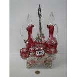 A six piece cranberry and clear glass condiment set on a plated stand.