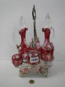 A six piece cranberry and clear glass condiment set on a plated stand.