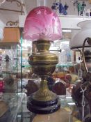 A Victorian brass oil lamp on black pot base with cranberry etched shade. COLLECT ONLY.