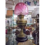 A Victorian brass oil lamp on black pot base with cranberry etched shade. COLLECT ONLY.