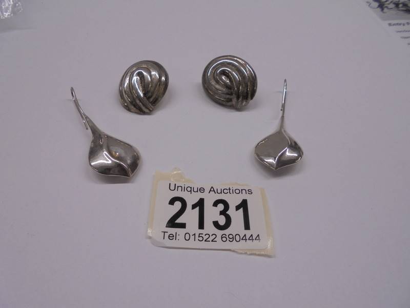 A pair of silver pendant earrings and a pair of silver stud earrings.