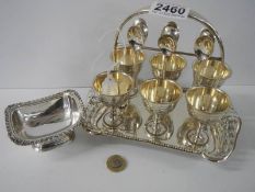 A silver plate egg cup stand with six silver spoons and a salt dish.