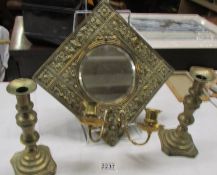 A brass framed mirror with candle sconces and a pair of brass candlesticks.
