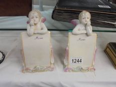 A pair of continental porcelain cherub menu figures.