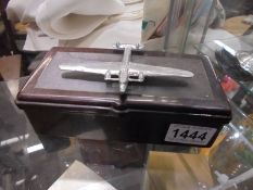 A vintage bakelite cigarette box with a white metal aircraft on top.