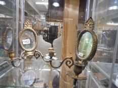 A pair of small brass wall mirrors with attached candle holders.
