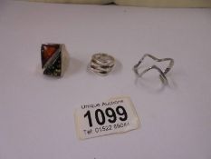 A silver ring set orange and green amber, another silver ring and an un-marked ring.